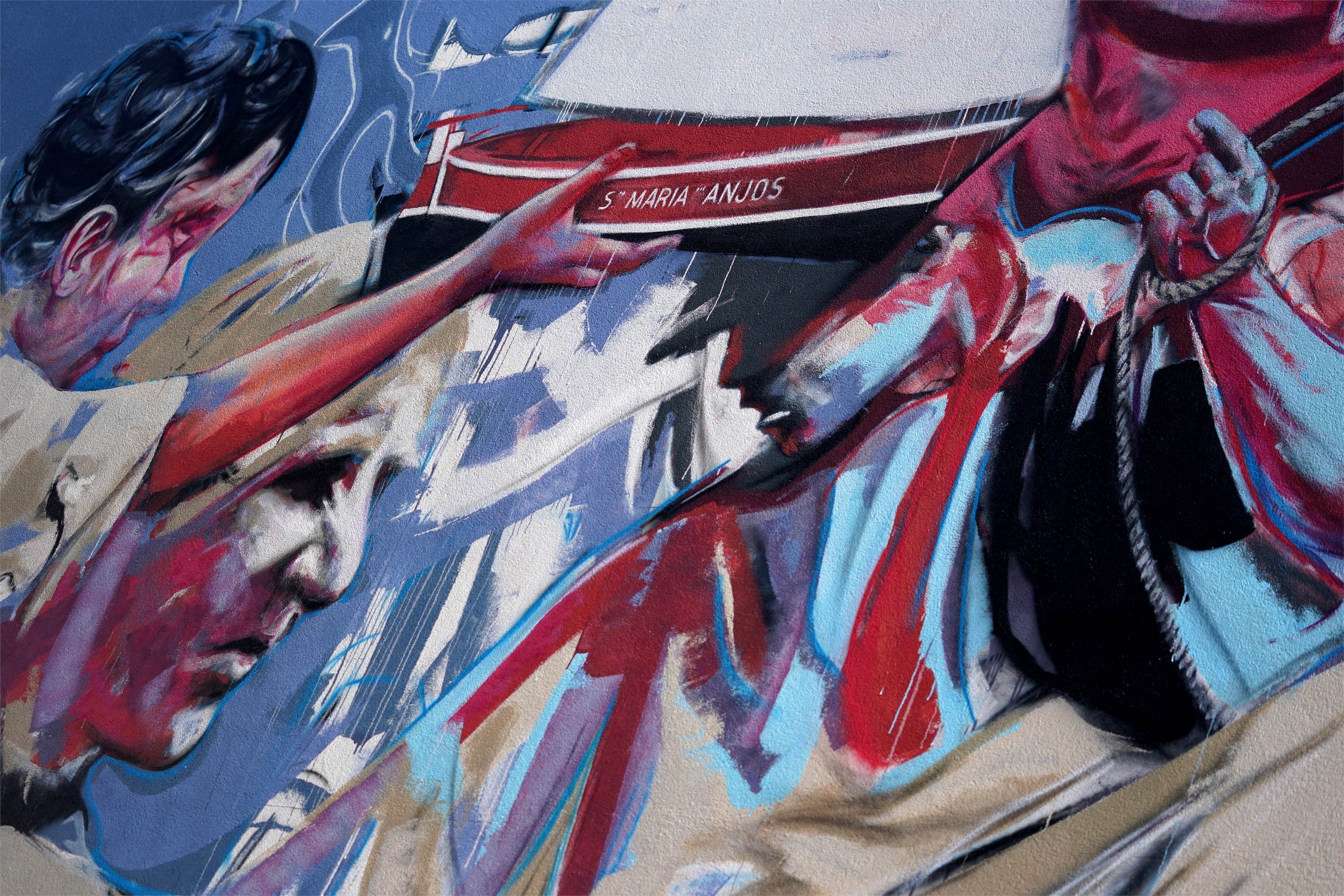 13.08.2022
No enquadramento da linguagem expressionista e do gesto, a pintura de Juan Domingues é um ato performativo e de contacto. A narrativa exposta é uma consequência da adaptação dos diálogos com a comunidade local, com o Museu Marítimo de Esposende e a Associação de Pescadores e parte de uma composição em pirâmide composta por 3 atos. Primeiro, temos a representação de São Pedro, padroeiro dos pescadores com valores cromáticos que simbolizam o nascer do sol. Depois, a representação poética da “regateira” com a criança ao colo a segurar uma catraia de Esposende, no intuito de representar e honrar o passado histórico da região, tanto como as gerações futuras. Este era um costume de infância antigo, que interessa lembrar. Temos ainda a ação da atividade piscatória, retratando-se os pescadores em esforço, notando-se o interior do barco com os pescadores a puxarem redes e cordas, intensificando-se a ação com o barco inclinado que representa o perigo e esforço da profissão. Por último, Juan Domingues contactou com um levantamento topográfico do século XIX que serviu de fundo e que estará representado como mapa de Esposende ao lado esquerdo de São Pedro e por detrás da mulher com a criança ao colo.